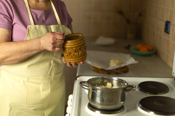 The hands of a senior woman add salt to sweet butter on the stove
