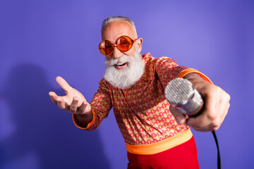 Charismatic senior man expressing joy with microphone in retro outfit, featuring a vibrant disco themed style and unique personality