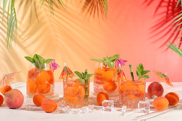 Iced peach tea or cocktail with mint and apricots, refreshing summer drink recipe. Two glasses with peach fruit lemonade on a light table, detox diet and weight loss concept, restaurant menu,