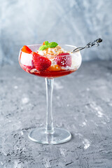 Ice cream with whipped cream, strawberries and peach in a glass tall glass on a gray background. Copyspace. Vertical photo.