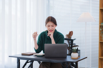 Focused Female Entrepreneur: A young woman sits at her desk, deeply engrossed in her work on a...