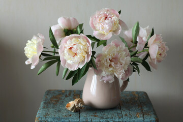 Pink and white peonies blooming in a vase on rustic table