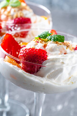 Ice cream with whipped cream, strawberries and peach in a glass tall glass on a gray background. Close-up. Vertical photo. Copyspace