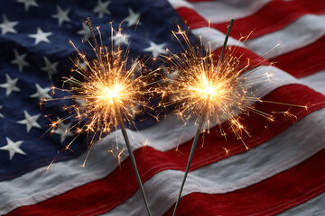 Two sparklers burning bright against American flag
