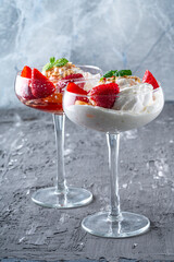 Ice cream with whipped cream, strawberries and peach in a glass tall glass on a gray background. Copyspace. Vertical photo.