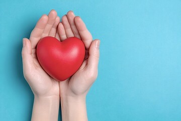 Obraz premium Female hands gently cradling a vibrant red heart against a soothing turquoise backdrop, representing love, care, and health in a minimalist and compassionate way