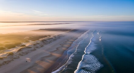 Aerial view of a beach with gentle waves and a misty horizon illuminated by soft sunlight creates a serene coastal landscape