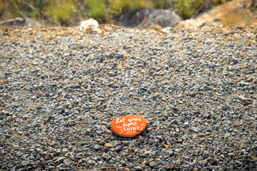 A hand painted Kindness Rock left on a gravel trail with Let Your Light Shine written in white on...