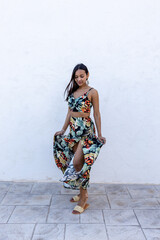 Woman in summer colored dress posing on a white wall.