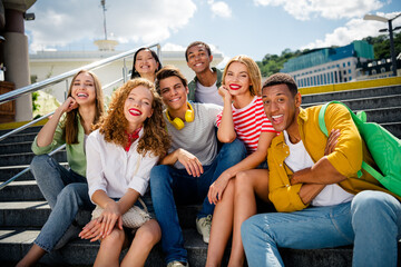 Obraz premium Group of joyful young friends relaxing on urban steps during a sunny day, enjoying summer, bonding