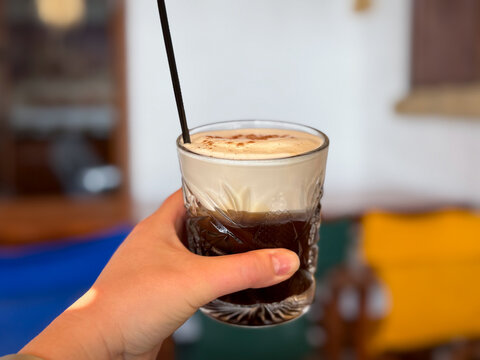 Glass of Freddo Cappuccino Greek iced coffee drink with espresso and cold frothy milk in female hand close up