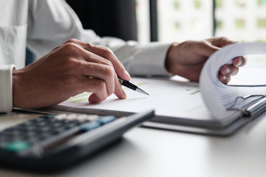 Focused businessman checking reports and verifying office documents with calculator and paper files on table