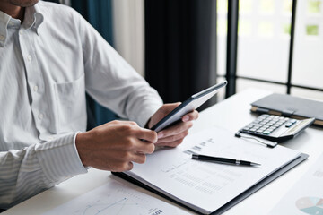 Businessman sitting at modern office desk using tablet device and checking paper documentห