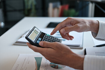 Administrative staff reviewing company budget report with calculator, document stack and focus at...