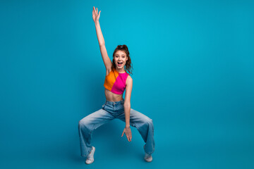 Energetic young woman in colorful top and jeans posing excitedly against a vibrant blue background