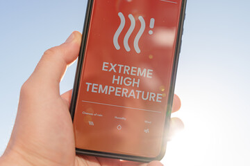 Smartphone screen showing extreme high temperature warning alert, hand holding phone under bright...
