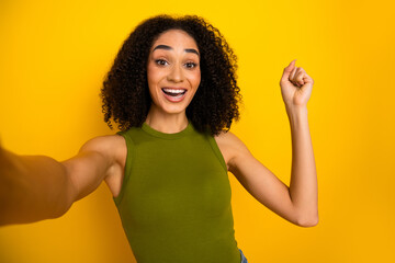 Cheerful young woman with curly hair posing joyfully against a vibrant yellow background, wearing a...