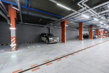 dimly lit, modern underground parking garage with cars, numbered spaces, and overhead pipes. Orange...