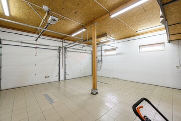 Bright garage interior with white doors, tiled floor, wood ceiling, support beam, and partial view...