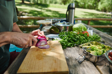 Person Preparing Vegetables on Wooden Cutting Board Outdoors for a Picnic Meal