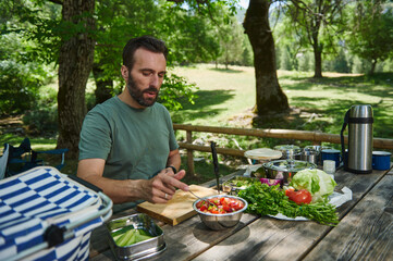 Man Preparing a Healthy Salad Outdoors at a Picnic Table Surrounded by Nature