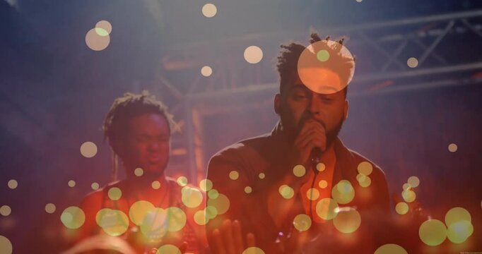 Male singer stepping into spotlight singing live music while guitarist nodding with bokeh overlay