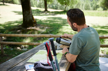 Man at a Scenic Outdoor Picnic Area Pouring Coffee with Hiking Gear Nearby