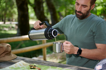 Man Pouring a Drink From a Thermos in a Wooden Outdoor Setting