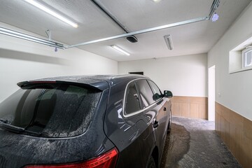 dark SUV is parked in a garage with white walls and ceiling, and tile accents. The floor is wet,...