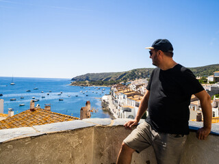 Latin man stands overlooking a picturesque coastal village and its serene harbor filled with boats....