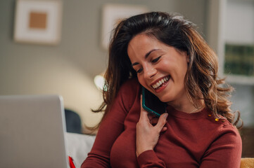 Happy freelancer woman talking on phone and working on laptop at home