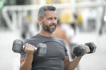 Sporty man lifting dumbbells outdoors. Sport man exercising with dumbbells in public outdoor gym....