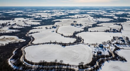 Obraz premium Aerial view of snow-covered landscape with winding dark lines and patches of forest under a clear sky emphasizing patterns and textures