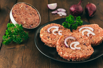 Three raw homemade burger meatballs and the burger press on wooden background