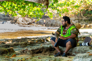 Local Costa Rican man in a Caribbean shirt resting under a tree with a recyclable water bottle on a beach in Cahuita National Park, Costa Rica