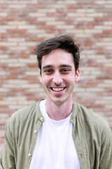 Vertical portrait of young adult man smiling at camera standing over city wall background. Cheerful...