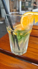 Refreshing lemonade with orange slice, mint leaves and ice cubes in a clear glass on a wooden table