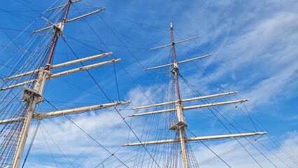 Tall ship masts and rigging set against a bright blue sky with light clouds, capturing maritime adventure and freedom. The image symbolizes exploration, travel and the spirit of the sea