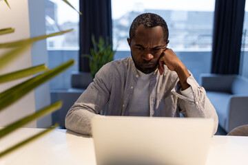African american man at the laptop looking thoughtful and serious