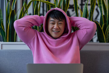 Asian young man in a pink hoodie at the laptop