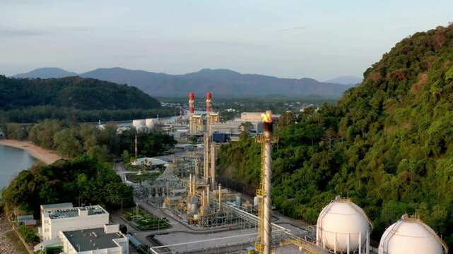 An industrial plant sits near the coast with mountains in the distance