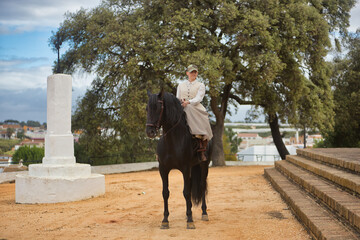 Young horsewoman riding a black Spanish thoroughbred horse, happy riding with him. She has saddle...