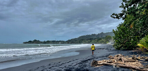 Junge in gelbem Trikot an einem schwarzen Strand in Puerto Viejo an der südlichen Karibik Küste...