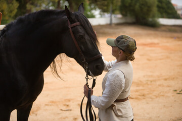 Portrait of young horsewoman caressing her black Spanish thoroughbred horse, with affection and...