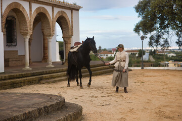 Young woman rider walking with her black Spanish thoroughbred horse, holding the reins. Concept...