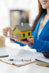 Real Estate Agent Presenting New Home: A smiling real estate agent offers a miniature yellow house...
