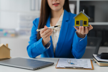 Real Estate Presentation: A business professional showcases a miniature house, poised to highlight...
