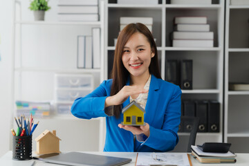 Successful Real Estate Agent: Confident professional in a stylish suit presents a miniature home,...