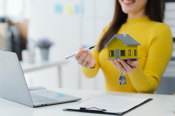 Dream Home Awaits: Smiling woman with pen showcases charming model house, symbolising exciting real...