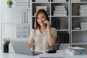 Obraz premium Asian Professional on Call: Radiant professional woman, engrossed in a mobile call at office desk. The scene exudes confidence, showcasing modern productivity amidst the company.